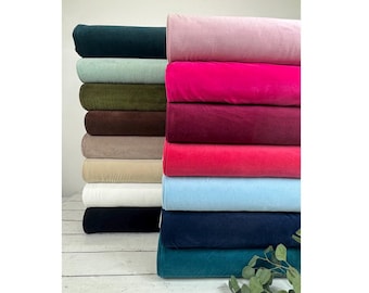 May include: A display of velvet fabric rolls in a range of colours, such as teal, light blue, pink, and burgundy. The rolls are stacked, highlighting the soft texture and rich colours of the material. The fabric is likely used for upholstery or clothing.