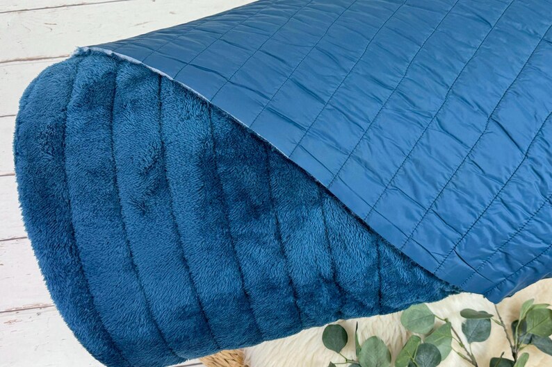 May include: A teal blue quilted fabric with a soft, plush texture on the reverse side. The fabric is folded in half, showing both sides.