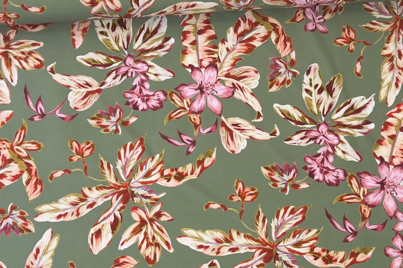May include: Green fabric with a floral pattern featuring pink flowers and white and red leaves.