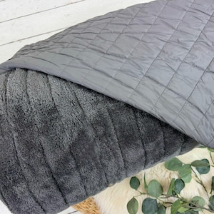 May include: A gray quilted blanket with a soft, plush side. The blanket is folded in half and the plush side is facing the camera.