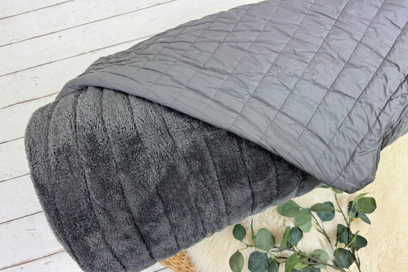 May include: A gray quilted blanket with a soft, plush side. The blanket is folded in half and the plush side is facing the camera.