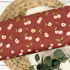 May include: Red fabric with a repeating pattern of pink cherries with green stems and leaves.