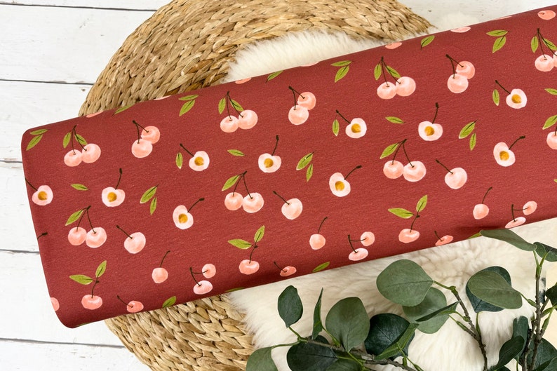 May include: Red fabric with a repeating pattern of pink cherries with green stems and leaves.