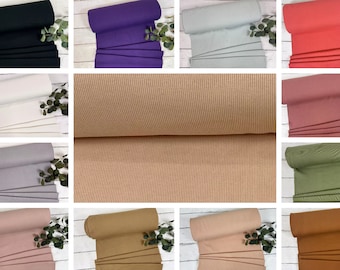 Könnte beinhalten: Eine Sammlung von 10 Rollen gerippten Stoffes in verschiedenen Farben, darunter Schwarz, Lila, Grau, Weiß, Beige, Rosa, Grün, Braun und Hellrosa. Der Stoff ist gerollt und auf einer weißen Holzoberfläche ausgestellt.