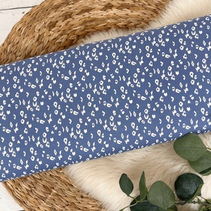 May include: A close-up of a blue fabric with a white leopard print pattern. The fabric is folded and lying on a woven surface.