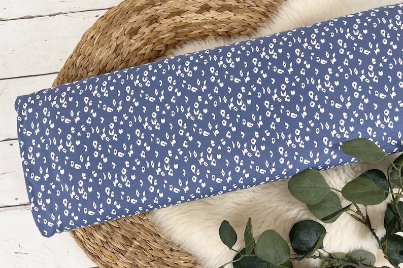 May include: A close-up of a blue fabric with a white leopard print pattern. The fabric is folded and lying on a woven surface.