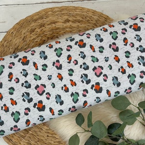 May include: White fabric with a colourful leopard print pattern. The print features black spots with accents of orange, pink, and green.