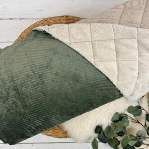 K&ouml;nnte beinhalten: Eine gesteppte Decke mit einer gr&uuml;nen Cordseite und einer cremefarbenen, pl&uuml;schigen Seite. Die Decke ist teilweise gefaltet und zeigt die verschiedenen Texturen und Farben. Ein geflochtener Korb und Gr&uuml;nzeug sind ebenfalls zu sehen.