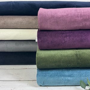 Könnte beinhalten: Ein Stapel verschiedener Cordstoffmuster in unterschiedlichen Farben. Die Farben umfassen Dunkelblau, Braun, Creme, Grau, Schwarz, Lila, Grün und Blau.