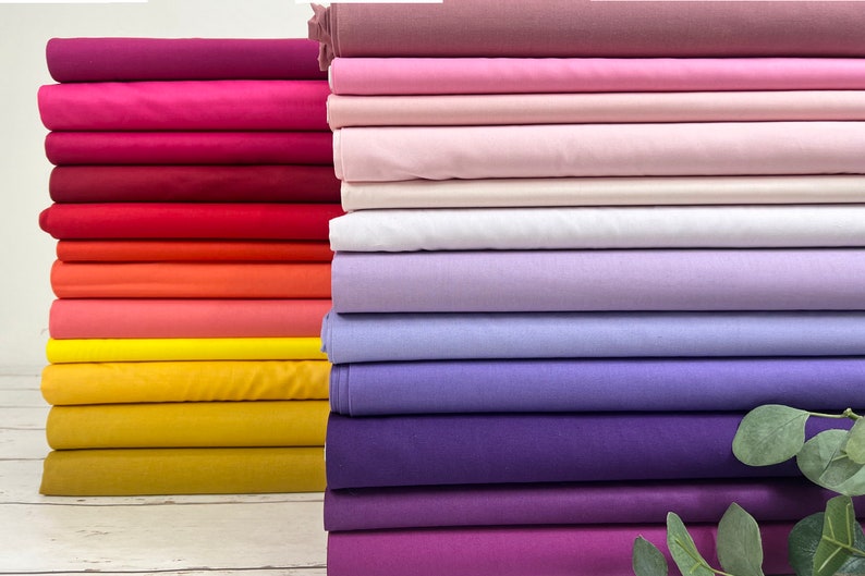 May include: A stack of colorful fabric swatches in shades of pink, purple, red, orange, and yellow. The fabric is smooth and appears to be cotton.