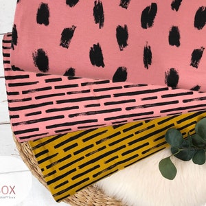 Peut inclure: Trois échantillons de tissu avec des motifs différents. L'échantillon du haut est rose avec des points noirs en forme de coups de pinceau. L'échantillon du milieu est rose avec des lignes horizontales noires. L'échantillon du bas est jaune avec des lignes horizontales noires.