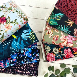 May include: A stack of colourful fabrics with tropical and floral patterns. The fabrics are arranged in a fan shape on a white wooden surface.