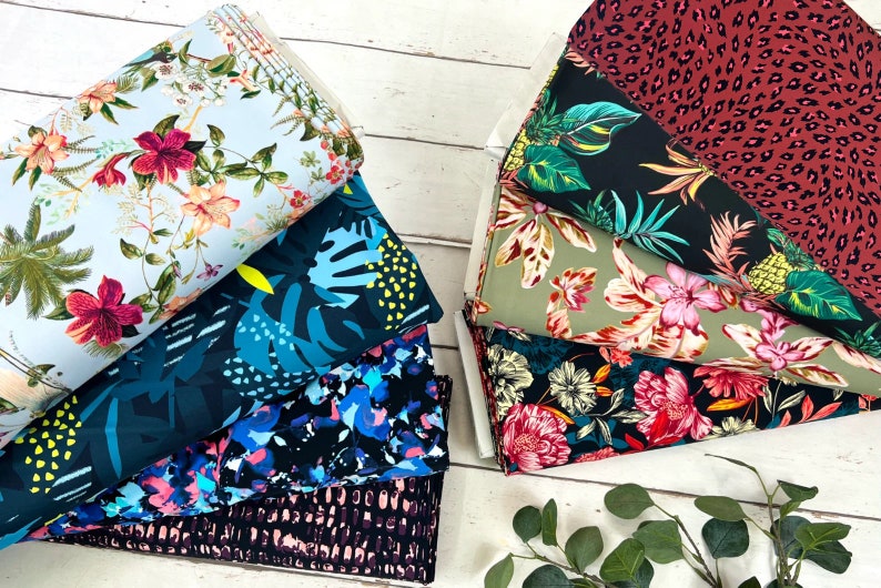 May include: A stack of colourful fabrics with tropical and floral patterns. The fabrics are arranged in a fan shape on a white wooden surface.