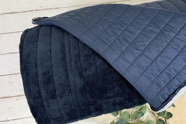 May include: A black and blue reversible pet bed. One side is made of a soft, plush fabric and the other side is a quilted fabric.