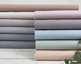 Puede incluir: Un conjunto de muestras de tela de diferentes colores, incluyendo beige, blanco, gris claro, lavanda, gris, azul claro y rosa. La tela es de textura suave y tiene un acabado acanalado.