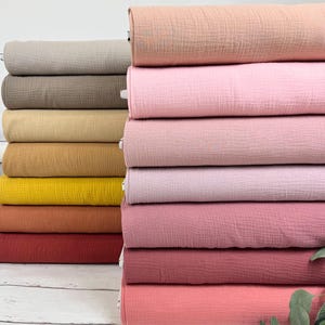 Può includere: Un assortimento di campioni di tessuto di diversi colori in varie tonalità di rosa, marrone, giallo, arancione e bianco. Il tessuto è un materiale morbido e gassoso con una superficie leggermente strutturata.