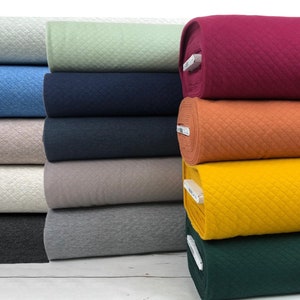 Puede incluir: Un rollo de tela en varios colores, incluyendo azul claro, beige, blanco, gris, gris oscuro, verde, amarillo, naranja, rojo y azul marino. La tela tiene una textura acolchada.