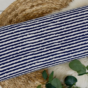 Pu&ograve; includere: Un tessuto bianco con strisce orizzontali blu navy. Le strisce hanno un effetto pennellato e usurato.