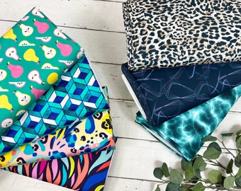 May include: A stack of colorful fabric swatches with various patterns, including pears, geometric shapes, animal prints, and abstract designs. The swatches are arranged on a white wooden surface.