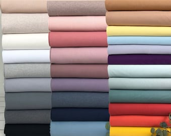 Könnte beinhalten: Ein Stapel verschiedenerfarbener Stoffrollen. Der Stoff ist ein weiches, dehnbares Strickmaterial. Die Farben umfassen Beige, Grau, Weiß, Rosa, Rot, Hellblau, Lila, Türkis, Grün, Orange und Gelb.