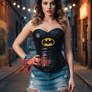 May include: Black sequined corset with a yellow Batman logo. The corset is strapless and paired with a denim skirt. The image also includes fishnet stockings and boots. The corset is from Corsets & More.