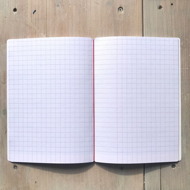 Puede incluir: Un cuaderno abierto con p&aacute;ginas cuadriculadas. Las p&aacute;ginas son blancas con un patr&oacute;n de cuadr&iacute;cula azul claro. La encuadernaci&oacute;n es roja y el cuaderno est&aacute; abierto sobre una superficie de madera clara.