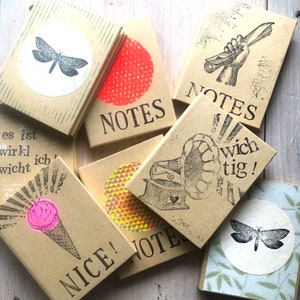 Könnte beinhalten: Eine Sammlung kleiner, brauner Notizbücher mit verschiedenen Designs. Die Notizbücher haben Titel wie "NOTES", "NICE!" und "wich tig!"  Einige Designs beinhalten einen Schmetterling, einen roten Kreis, ein geometrisches Muster und einen Vintage-Plattenspieler.