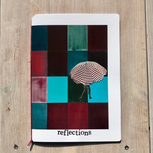Puede incluir: Un cuaderno con un dise&ntilde;o abstracto y colorido. La portada presenta una cuadr&iacute;cula de cuadrados en tonos de rojo, verde azulado y verde oscuro. Una figura con un paraguas est&aacute; superpuesta a la cuadr&iacute;cula. La palabra "reflections" est&aacute; impresa en la parte inferior.