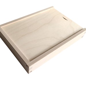 Puede incluir: Una caja de madera simple con una tapa con bisagras. La caja está hecha de madera clara y tiene un acabado natural.
