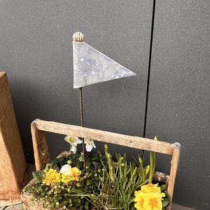 Könnte beinhalten: Eine rustikale Holzkiste mit gelben und weißen Blumen und Grünzeug. Eine kleine Metallfahne ist an der Kiste befestigt. Die Kiste hat einen Griff zum einfachen Tragen.