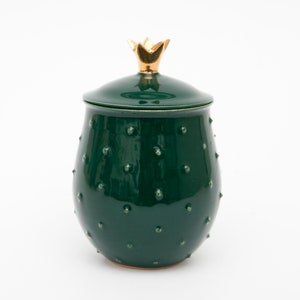 May include: A green ceramic jar with a gold crown lid. The jar has a textured surface with small bumps.