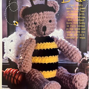 Puede incluir: Un oso de peluche Bumblebee Bear hecho a mano con ganchillo. El oso tiene cabeza, brazos y piernas marrones, con un cuerpo a rayas negras y amarillas. Cuenta con alas blancas, antenas y el texto "Bumblebee Bear". El oso de peluche está totalmente articulado.