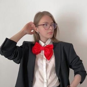 May include: A woman wearing a black blazer, a white collared shirt, and a large red bow tie.