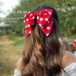 May include: A red and white polka dot bow hair clip. The bow is tied in a large, full shape.