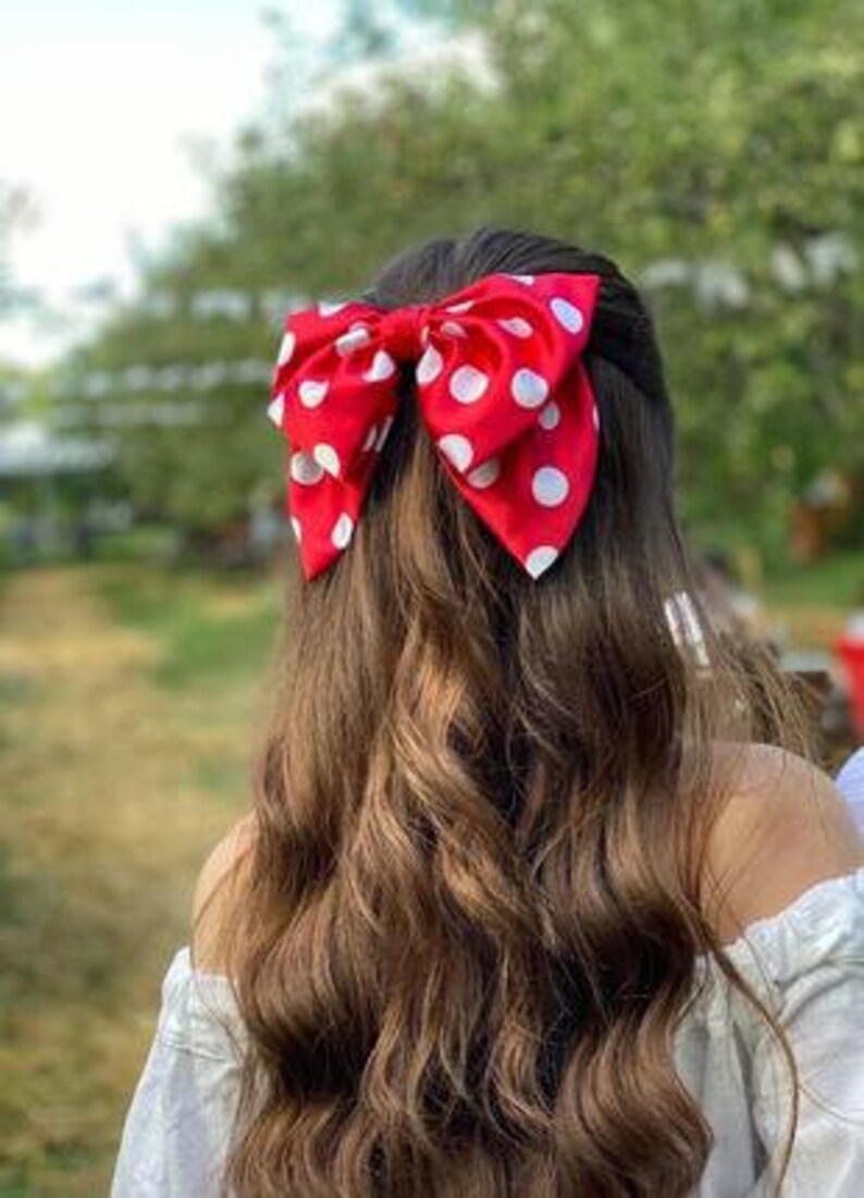 May include: A red and white polka dot bow hair clip. The bow is tied in a large, full shape.
