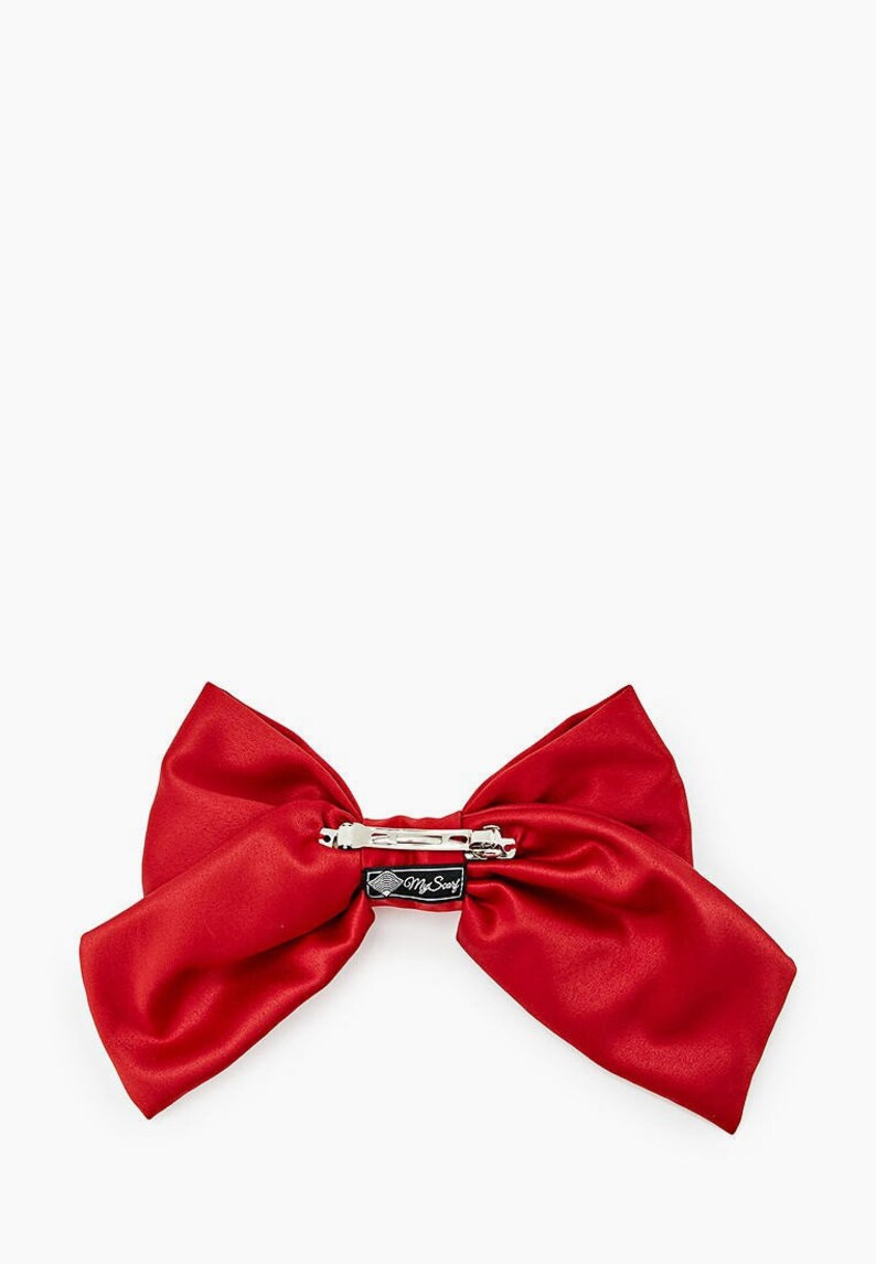 May include: A large red satin bow with a silver clip. The bow has a black tag with the text "My Swag" on it.