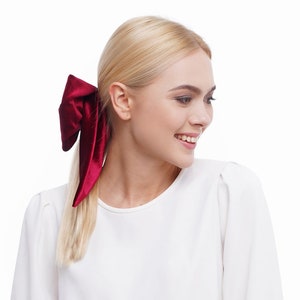 May include: A woman with blonde hair wearing a white shirt with a burgundy velvet bow in her hair.