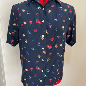 Op de afbeelding: Een donkerblauw overhemd met korte mouwen, een knoopsluiting aan de voorzijde en een herhalend bloemenpatroon in de kleuren rood, geel en paars. Het overhemd heeft een klassieke kraag, een knoopsluiting met lichte knopen en een rechte zoom.