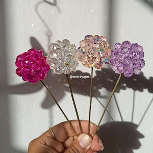 Op de afbeelding: Vier parelbloemstelen met roze, witte en paarse iriserende parels. De stelen worden in een hand gehouden.