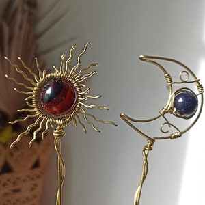 Könnte beinhalten: Goldene Drahtskulpturen von Sonne und Mond mit roten und blauen Edelsteineinsätzen.