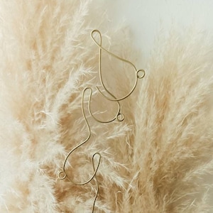 May include: A gold wire sculpture of the word "&" against a backdrop of beige pampas grass.