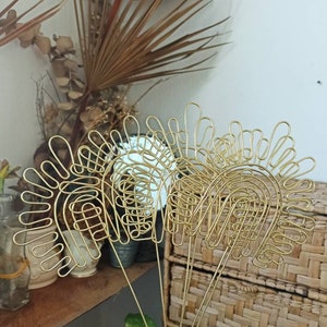 Pu&ograve; includere: Set di tre sculture in filo dorato a forma di archi con un design ondulato decorativo. Le sculture sono disposte a ventaglio e sono tenute nella mano di una persona.