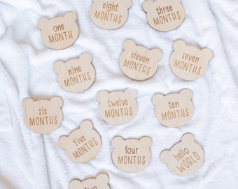 May include: Twelve wooden bear-shaped baby milestone cards with text that reads "one month", "two months", "three months", "four months", "five months", "six months", "seven months", "eight months", "nine months", "ten months", "eleven months", "twelve months", and "hello world".