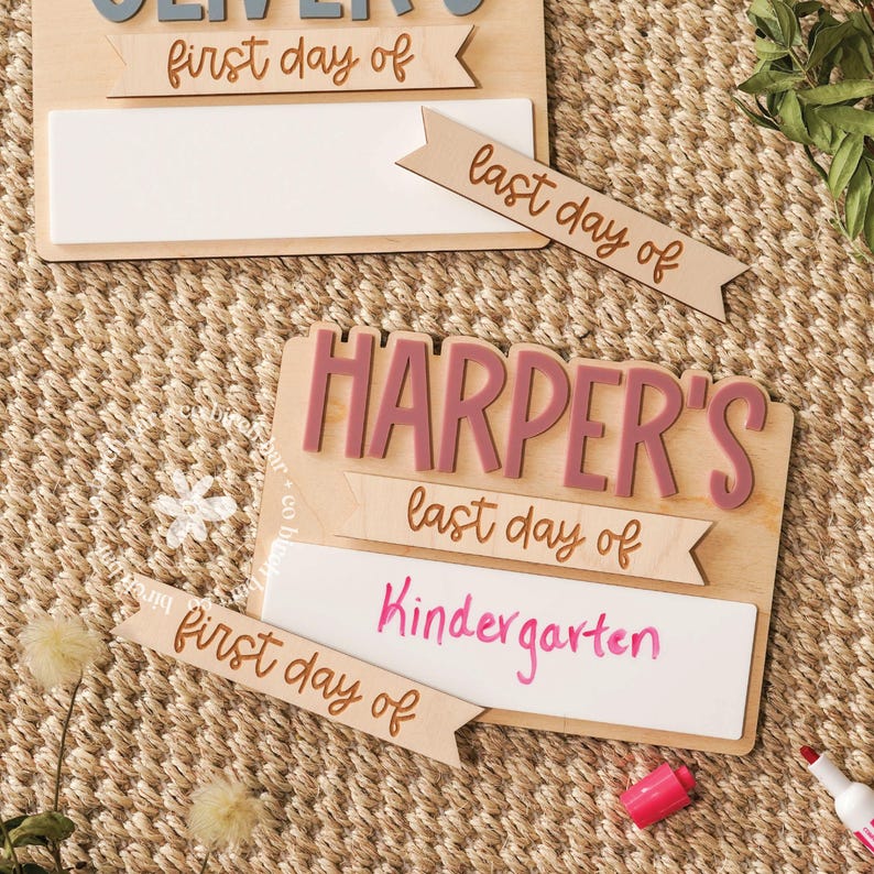 May include: Wooden school sign with the name "Oliver" in blue and "Harper's" in pink. The signs have banners that read "first day of" and "last day of Kindergarten". The background is a woven texture.