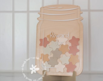 Pode incluir: Um pote de recompensa de madeira com acabamento marrom claro. O pote tem a forma de um pote de pedreiro e tem uma inscrição branca que diz "Reward Jar". O pote está cheio de pequenas fichas em forma de estrela em tons de rosa, bege e marrom.