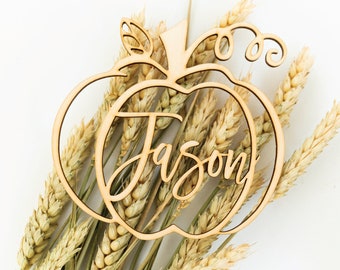 May include: Wooden pumpkin cutout with the name Jason written in cursive inside. The pumpkin is surrounded by wheat stalks.