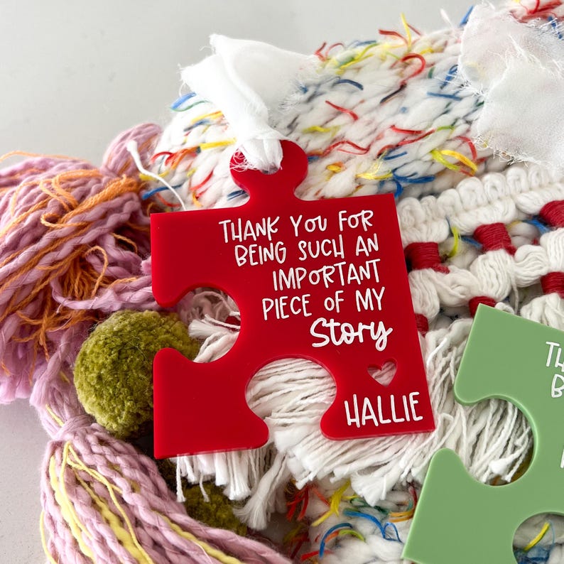 May include: Red puzzle piece shaped acrylic ornament with the text "Thank you for being such an important piece of my story" and the name "Hallie" at the bottom.