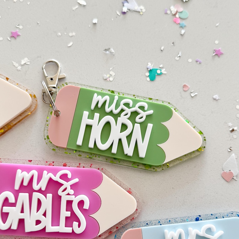 Pode incluir: Chaveiro em forma de l&aacute;pis verde, rosa e branco com o texto "miss HORN" em letras brancas.