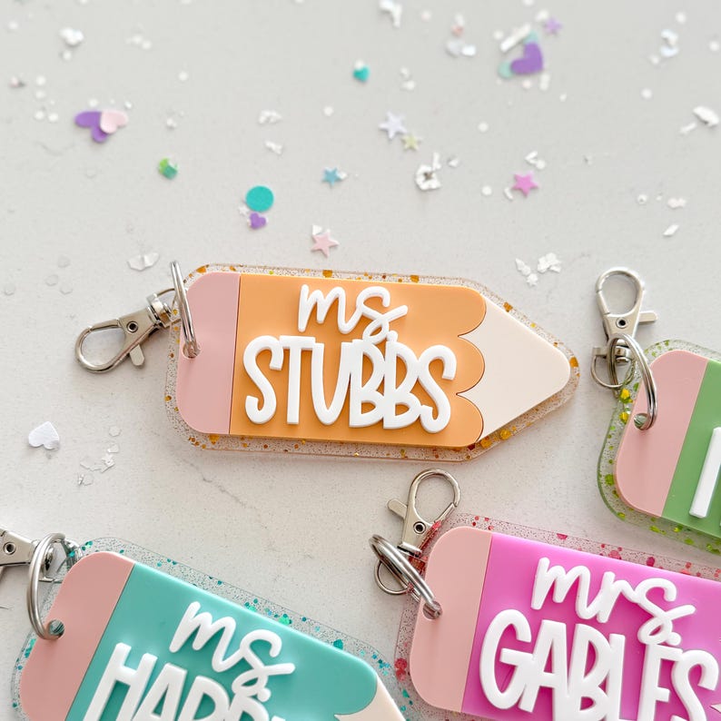 Pode incluir: Quatro chaveiros em forma de l&aacute;pis coloridos com detalhes de glitter. Cada chaveiro tem o nome de um professor diferente: "Ms. Stubbs", "Ms. Harris", "Mrs. Garbles" e "Mrs. [nome ileg&iacute;vel]".
