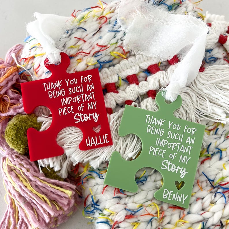 May include: Two red and green puzzle-shaped ornaments with white text that reads "Thank you for being such an important piece of my story." The red ornament has the name "Hallie" and the green ornament has the name "Benny".